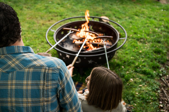 photo of a father and daughter roasting sausages together over a grill