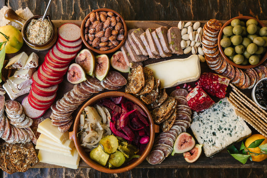 a large charcuterie board featuring figs, pickles, olives, cured meats and sausages