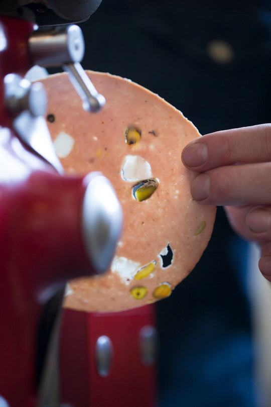 Mortadella being sliced on the slicer with light pouring through.