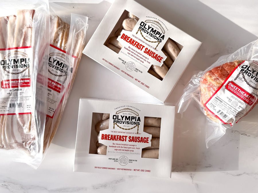 two packs of olympia provisions breakfast sausage and uncured bacon and an olympia provisions sweetheart ham