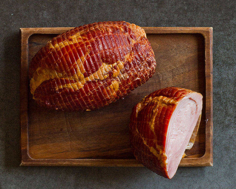 a whole and half sweetheart ham on a wood cutting board