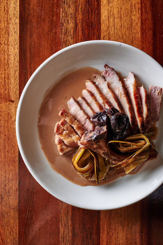 Cooked pork belly and vegetables plated in a white bowl.