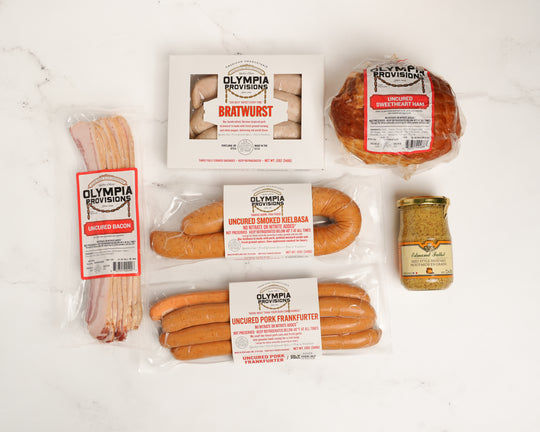 Assorted Olympia Provisions sausages, ham, bacon, mustard on a white surface