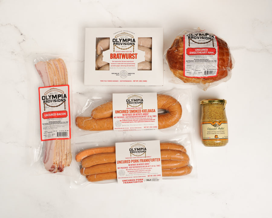 Assorted Olympia Provisions sausages, ham, bacon, mustard on a white surface
