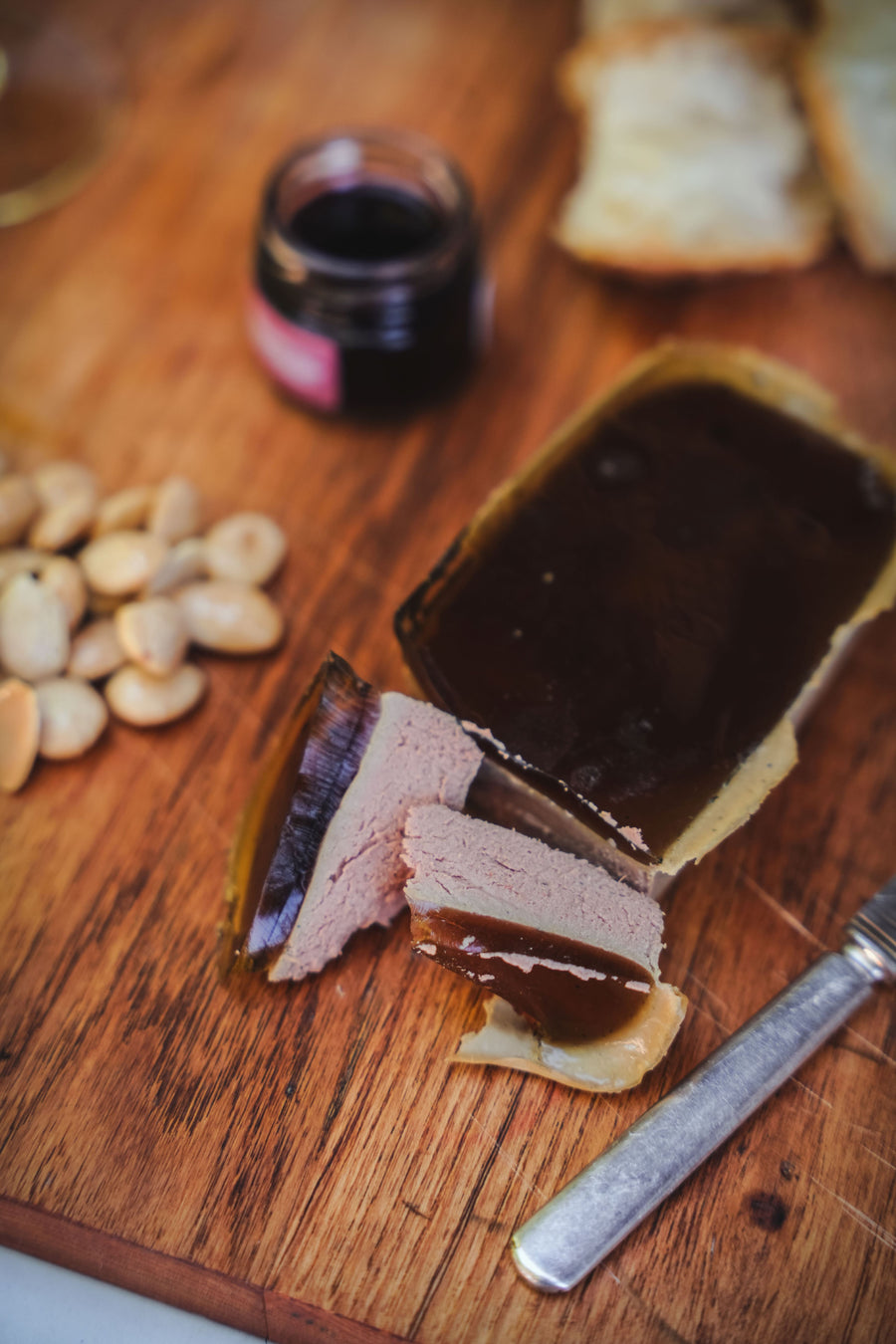Sliced terrine with a dark filling on a wooden board with nuts and a jar of red wine.
