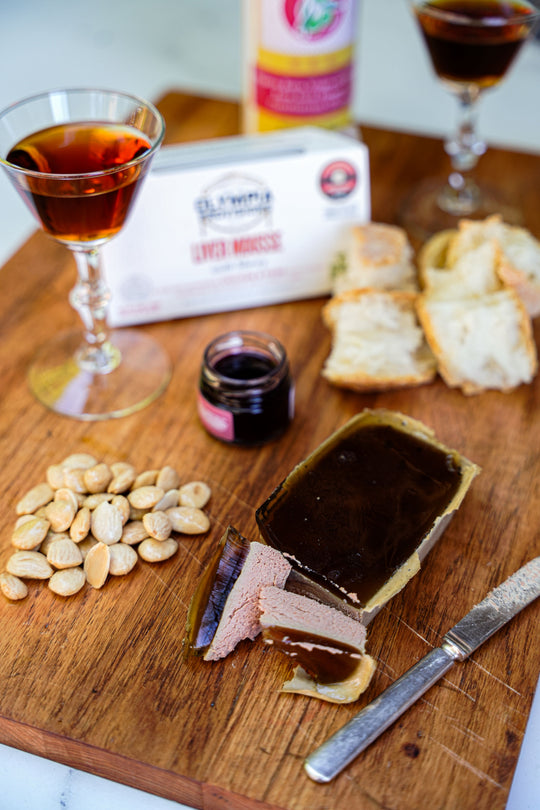 Wooden board with sliced terrine, crackers, nuts, and a glass of red wine.