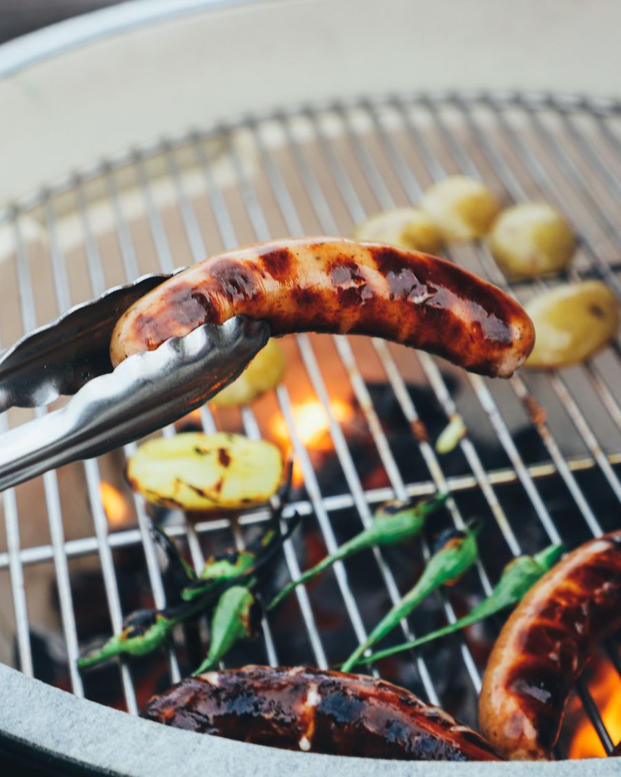 Tongs picking up a bratwurst with a grill
