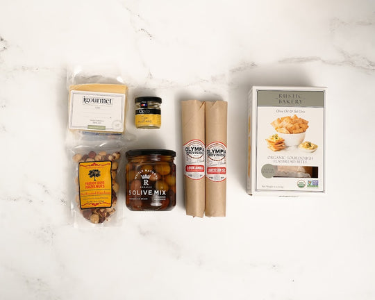 Assorted salami, cheese, olives including a jar, a box, and two packages on a white marble surface.