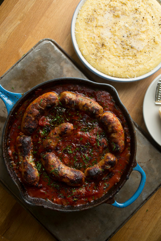 a frying pan with chorizo in tomato sauce next to a bowlof polenta
