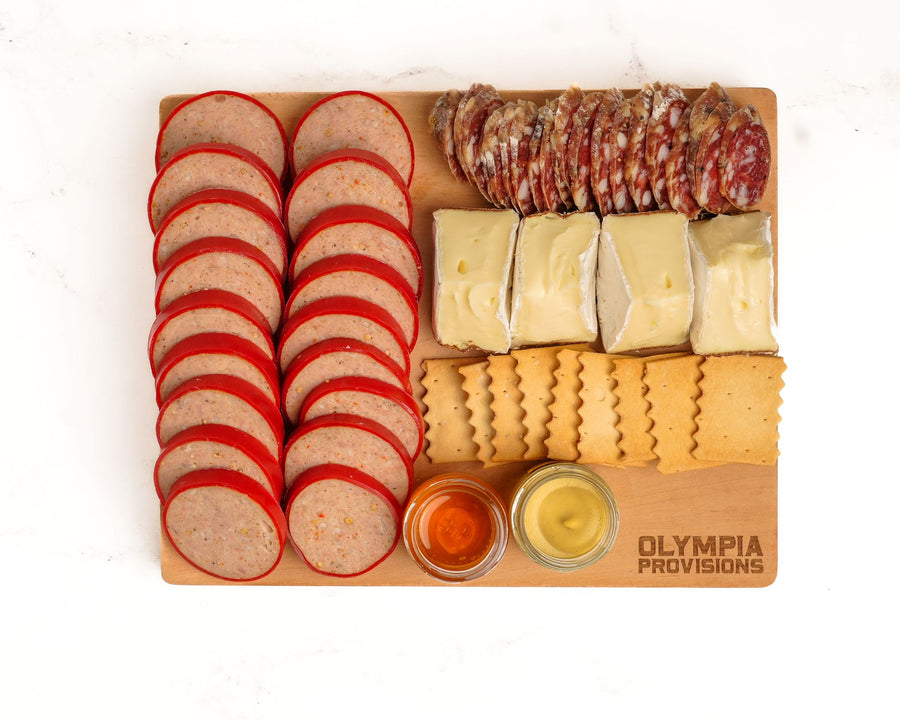 Wooden charcuterie board with sliced salami, summer sausage,, cheeses, and crackers on a white background.