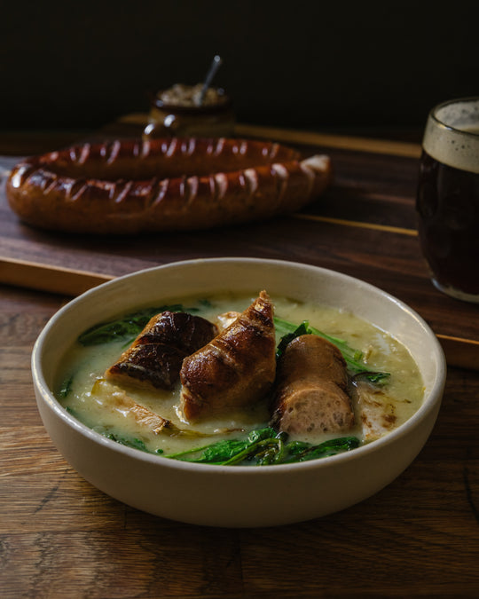 Kielbasa on a board with a beer and a bowl of soup with kielbasa