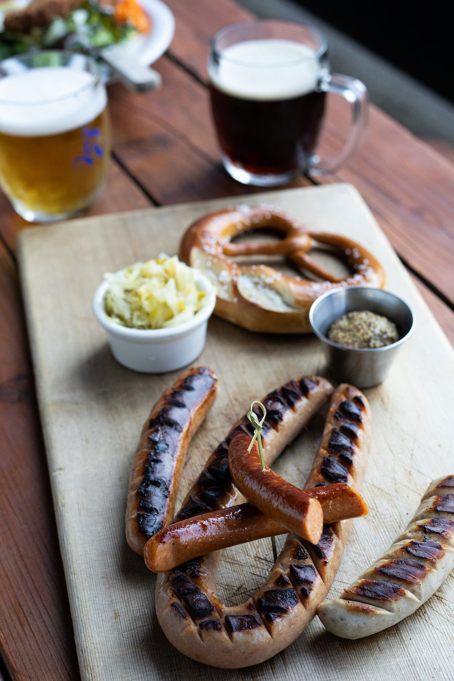 sausages on platter with kraut, mustard, pretzel and beer