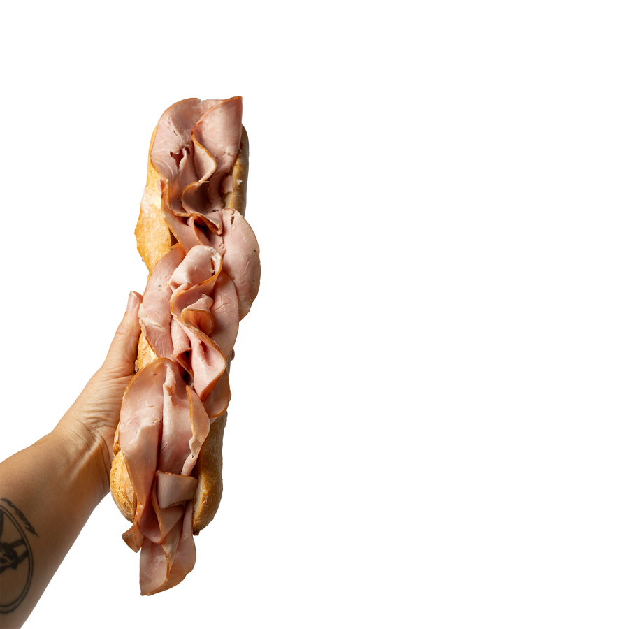 A hand holding a baguette filled with sliced pink ham, isolated on a white background.