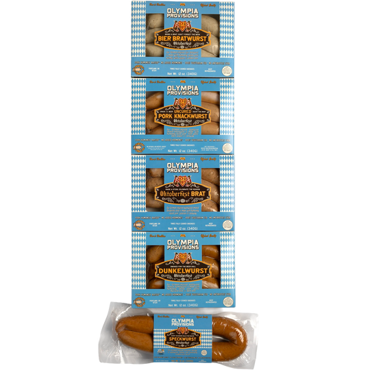 Five packages of Olympia Provisions Oktoberfest sausages stacked vertically in blue and white packaging. from top to bottom: Bier Bratwurst, Pork Knackwurst, Oktoberfest Brat, Dunkelwurst, and Speckwurst.