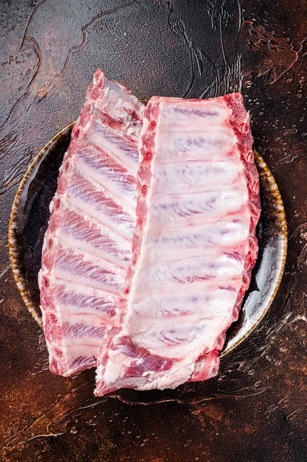 Two racks of baby back ribs in a ceramic bowl on a dark brown background