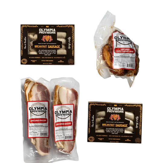 Two packs of Olympia Provisions Breakfast Sausage in black packaging, one uncured sweetheart ham, and two packs of uncured bacon.