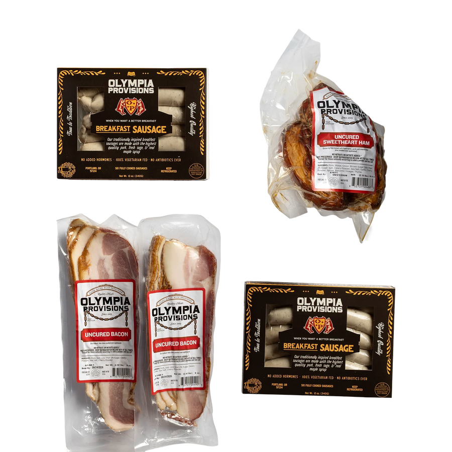 Two packs of Olympia Provisions Breakfast Sausage in black packaging, one uncured sweetheart ham, and two packs of uncured bacon.