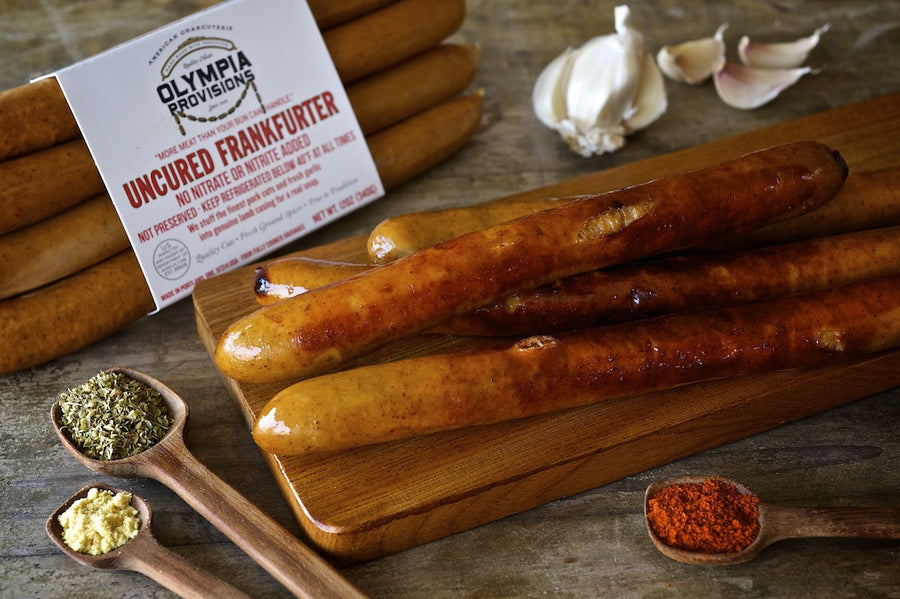 Olympia Provisions uncured Frankfurters in a package and laid out on a board